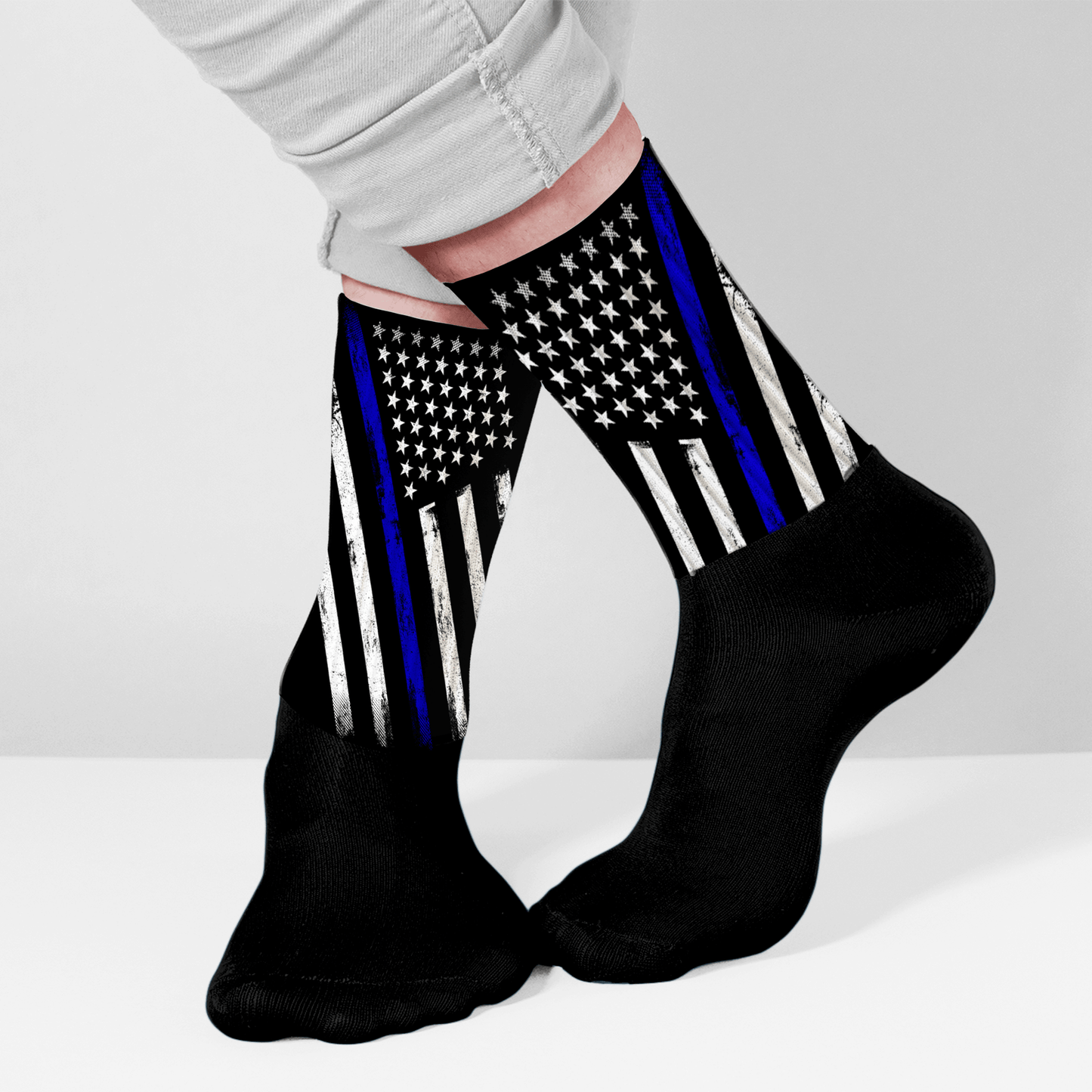 Black socks with American flag design featuring a blue stripe, worn by a person on a light gray background.