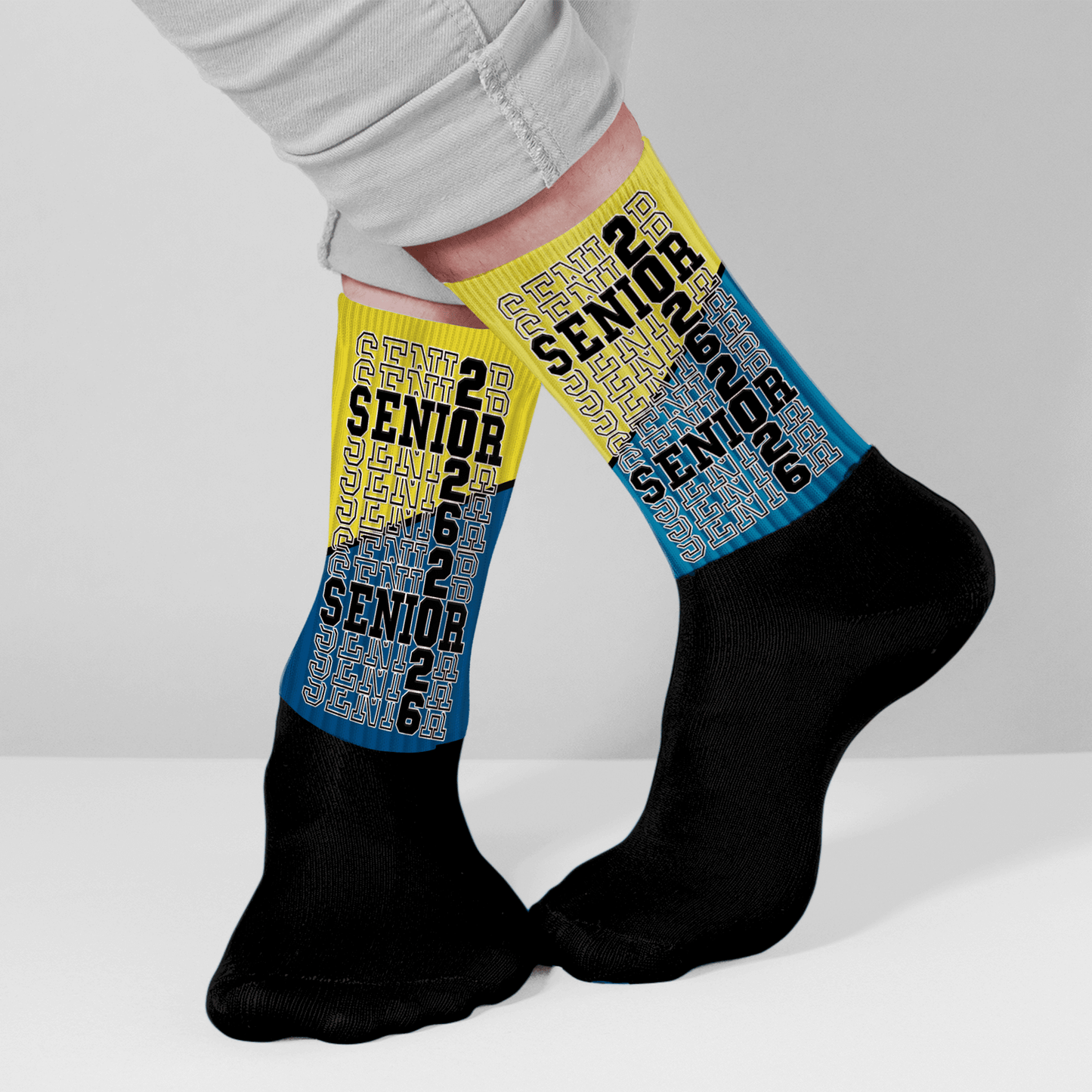 Person wearing black socks with yellow and blue '2 Senior 2' socks on a light gray background