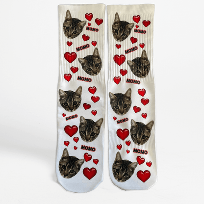 Pair of socks with cat faces and red hearts on a white background